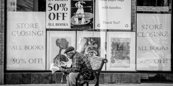 Man sitting on bench in front of store that is closing.