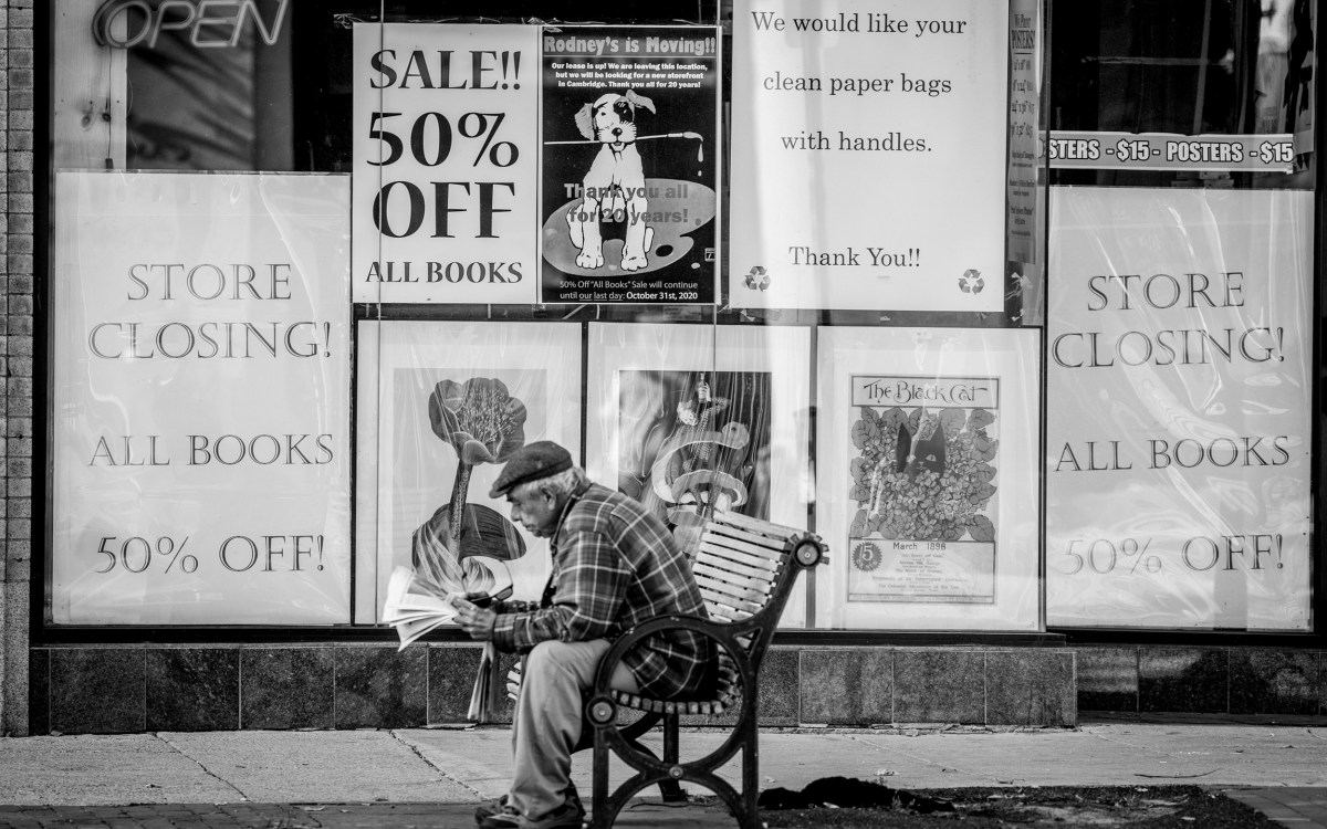 Man sitting on bench in front of store that is closing.