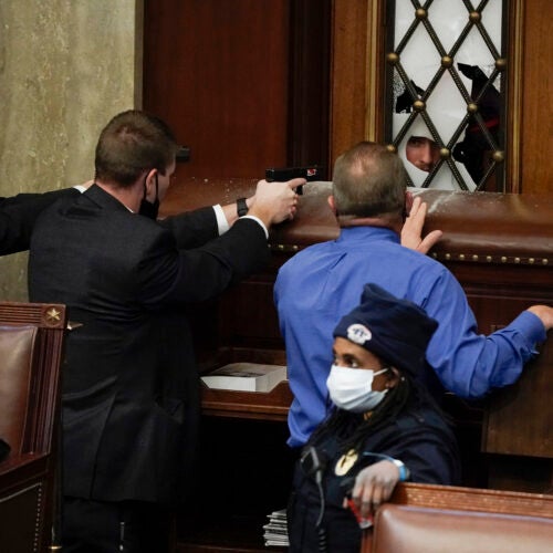 Police with guns drawn watch as rioters try to break into the House Chamber.