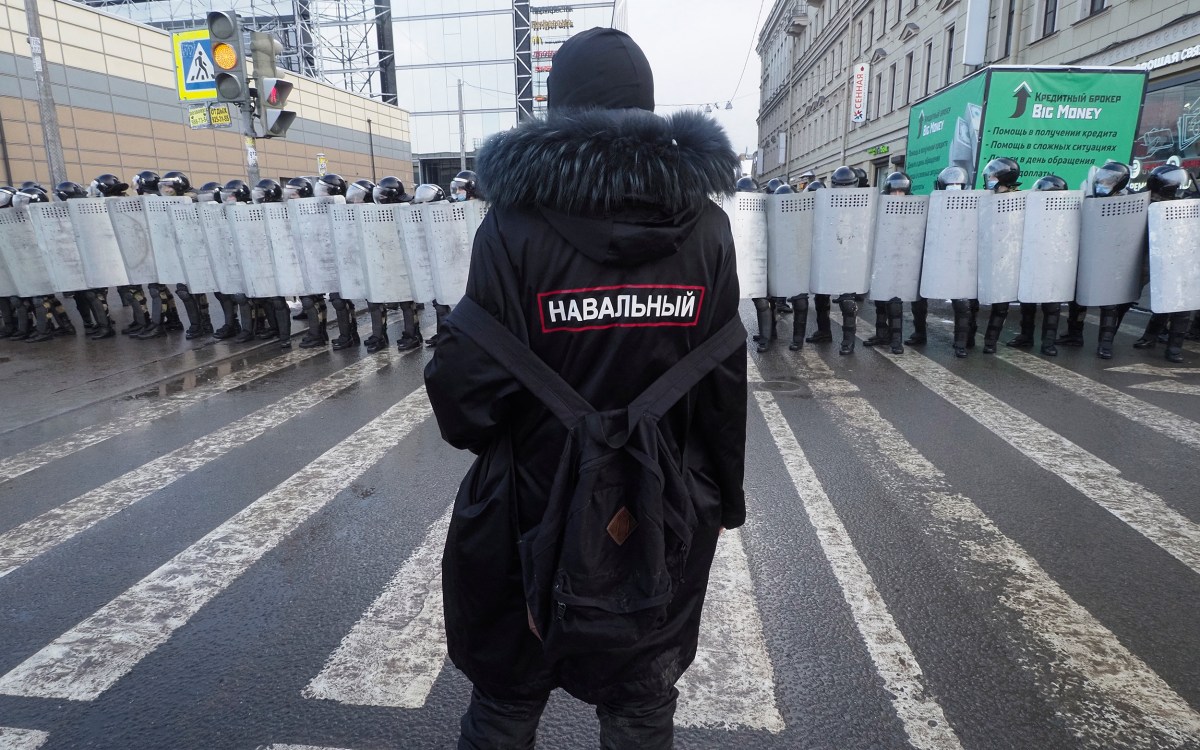 A man with a sign 'Navalny' on his back stands in front of riot policeme.