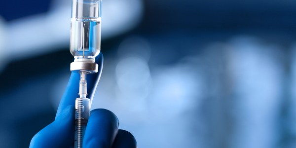 A medical hand in a glove holds an ampoule with a vaccine and a syringe with illustration