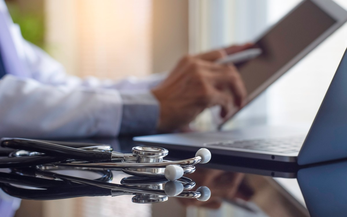 Male doctor in white coat hand holding and using modern digital tablet.