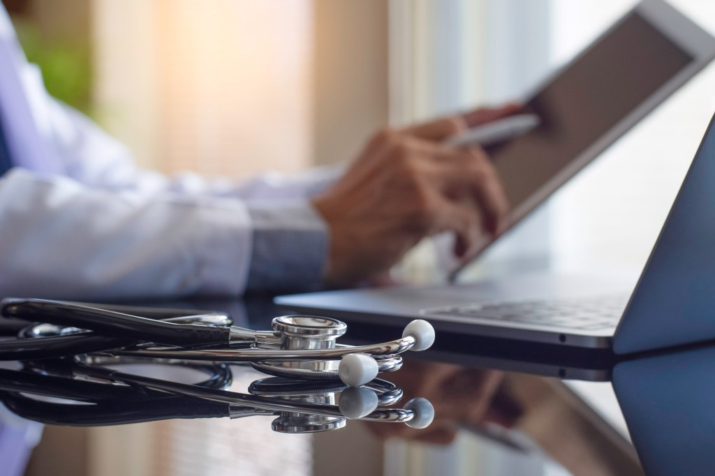 Male doctor in white coat hand holding and using modern digital tablet.