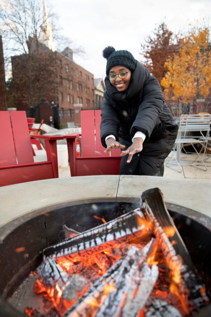 Alaa Hamid, a Graduate School of Design student, warms hands by a fire pit.