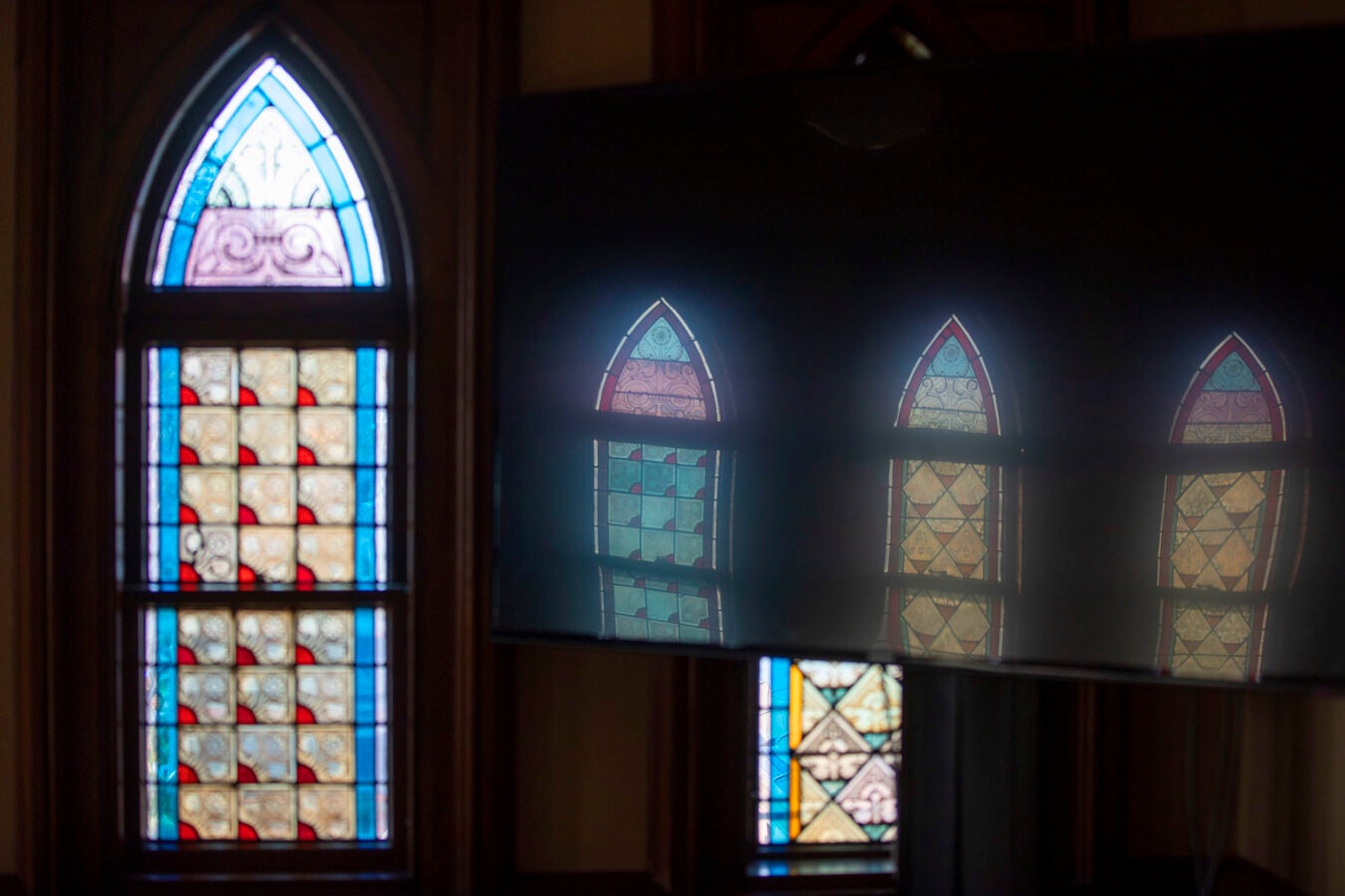 Stained-glass windows cast a reflection on an overhead monitor in Memorial Hall.