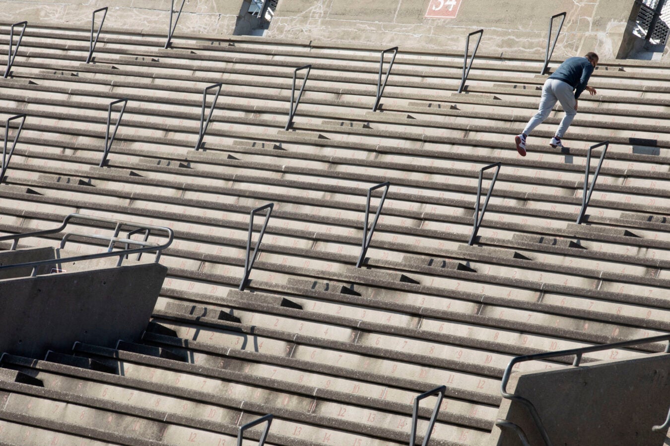 A dogged runner ascends the steep grid of Harvard Stadium stairs.