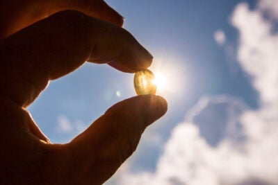 Vitamin D capsule against blue sky with sunshine.