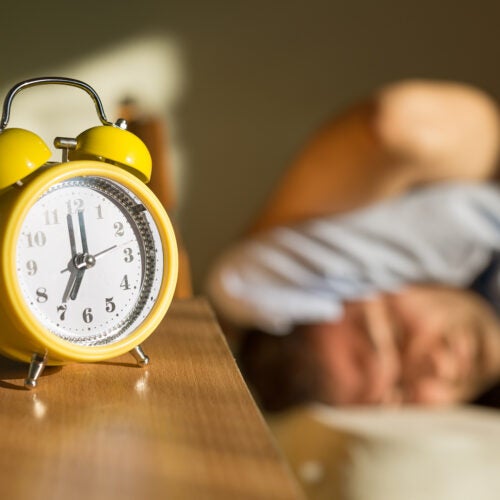 Person sleeping disturbed by alarm clock.