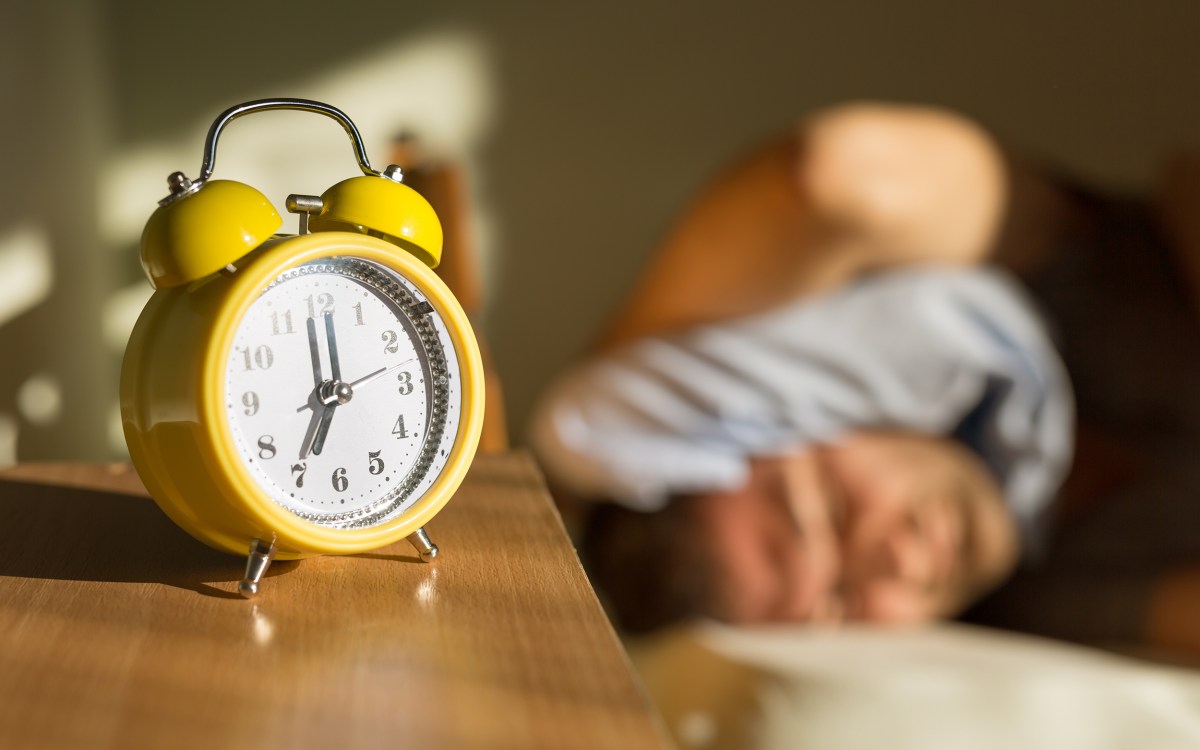 Person sleeping disturbed by alarm clock.