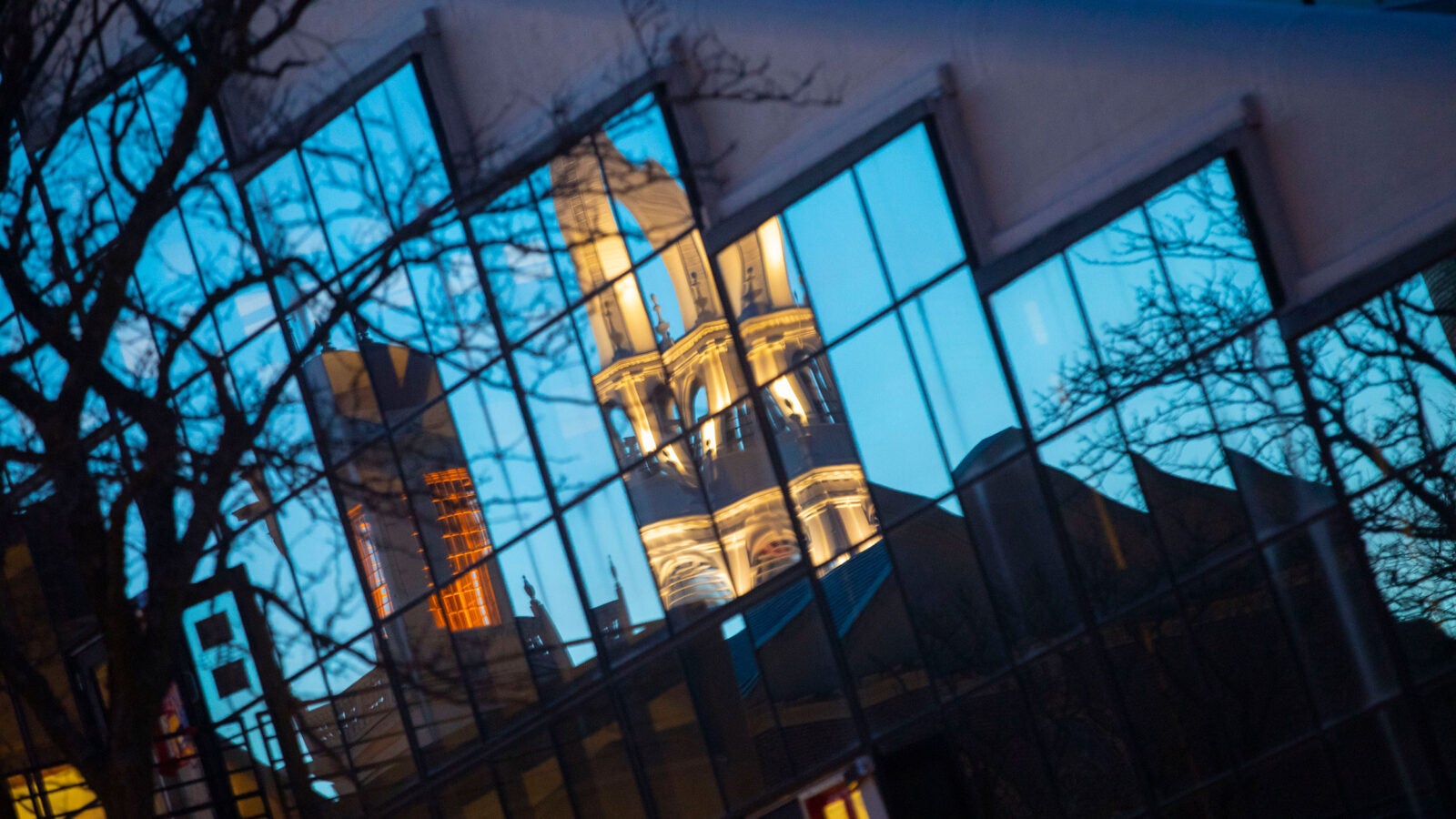 Gund Hall is seen reflecting the tower of Memorial Church at sunset.