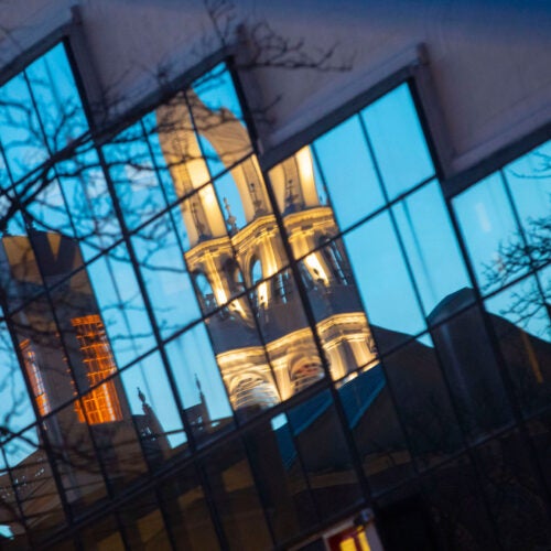 Gund Hall is seen reflecting the tower of Memorial Church at sunset.