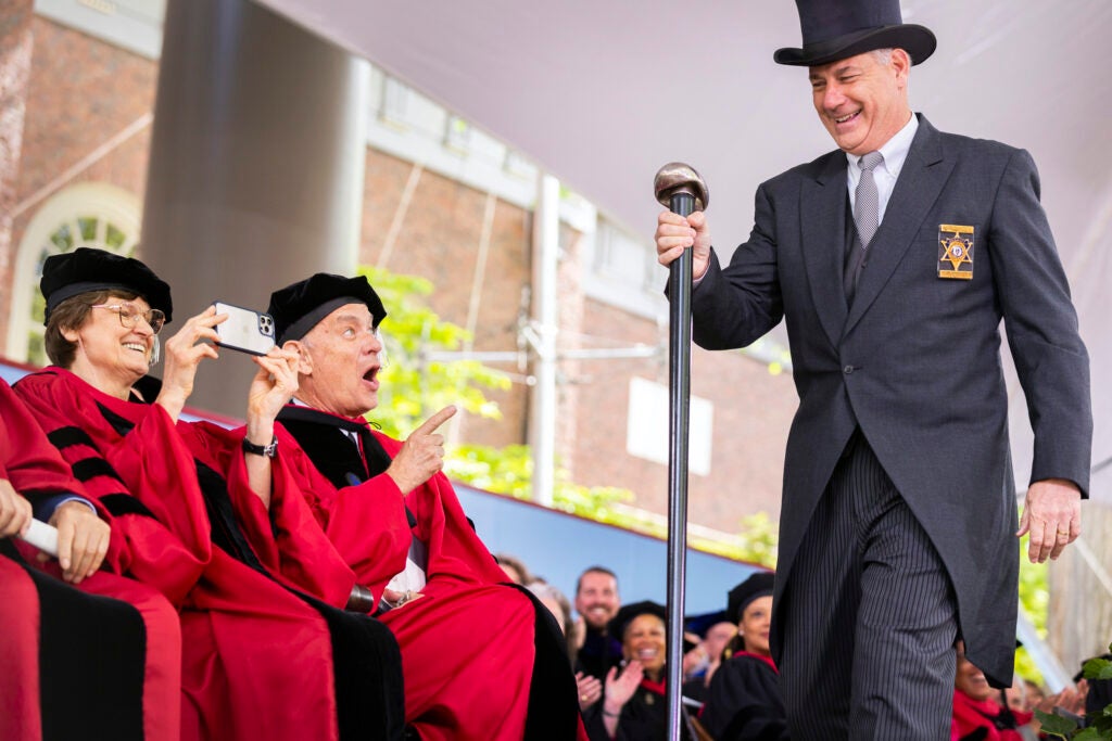 Katalin Karikó takes a photo with phone and Tom Hanks points as Peter J. Koutoujian calls Commencement to order.