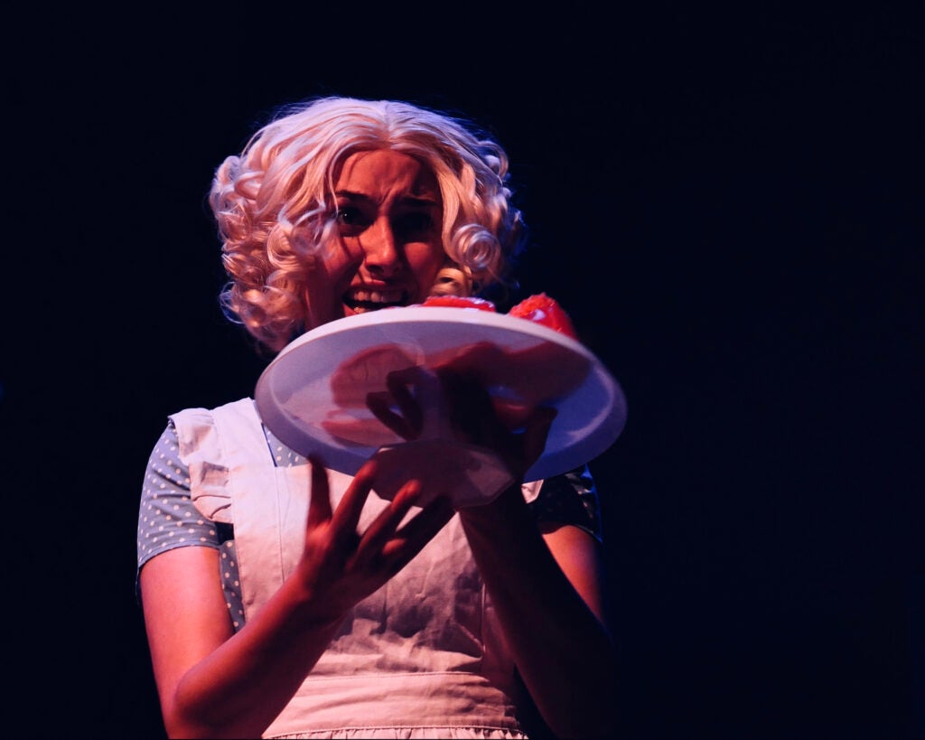 Alyse Clinton as Aiden in "SWAN," donning an apron, holds Jell-O on a plate.