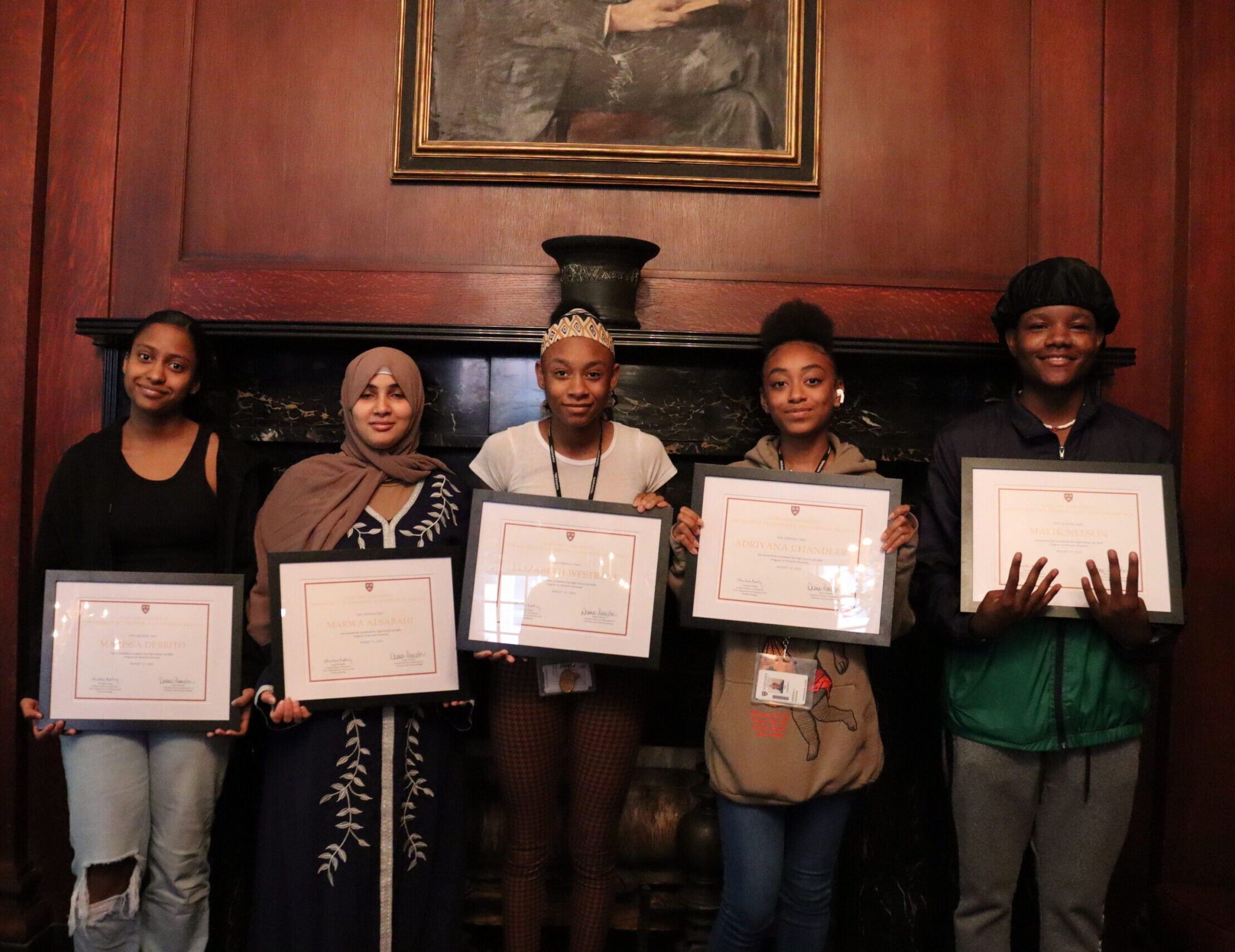 Brighton High School students Marissa Debrito, Marwa Alsabahi, Elizabeth West Raye, Adriyana Chandler, and Malik Nelson hold their certificates of completion in front of a fireplace for the 2nd annual CCB High School Lab Skills summer internship program.
