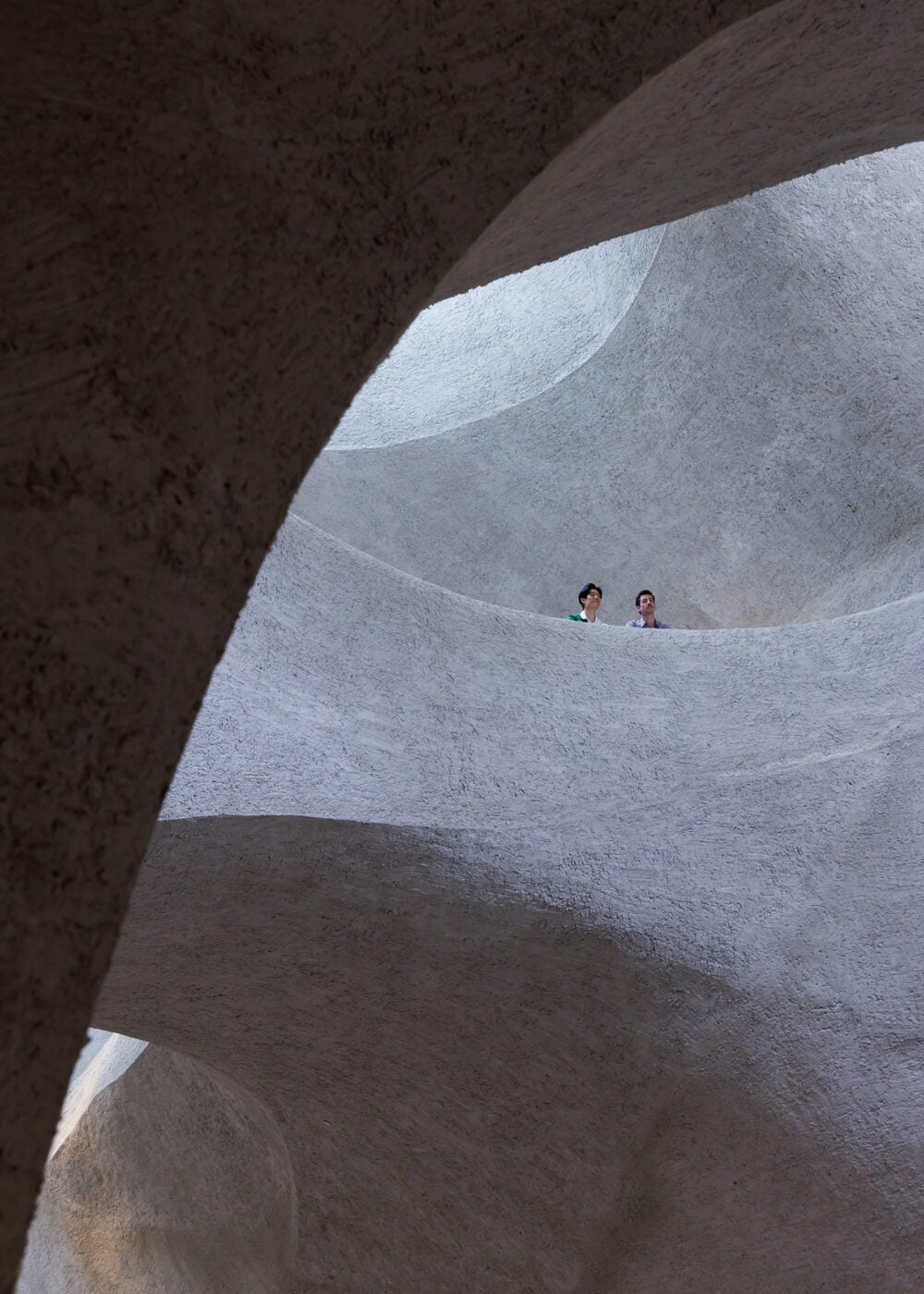 Two people look down from Gilder Center bridge as lights and shadows make upper floors appear cavernous.
