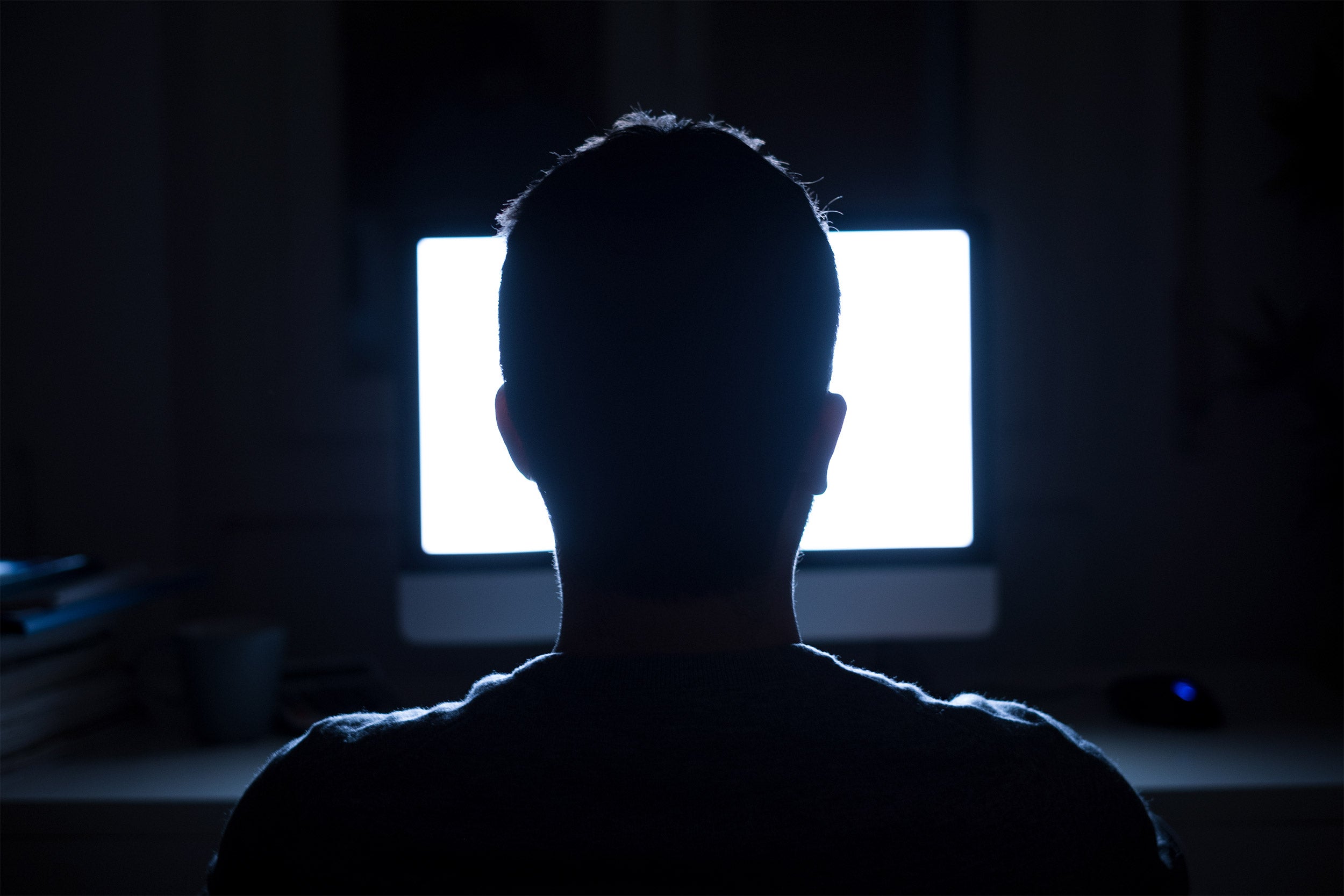Silhouette of man's head in front of computer monitor.
