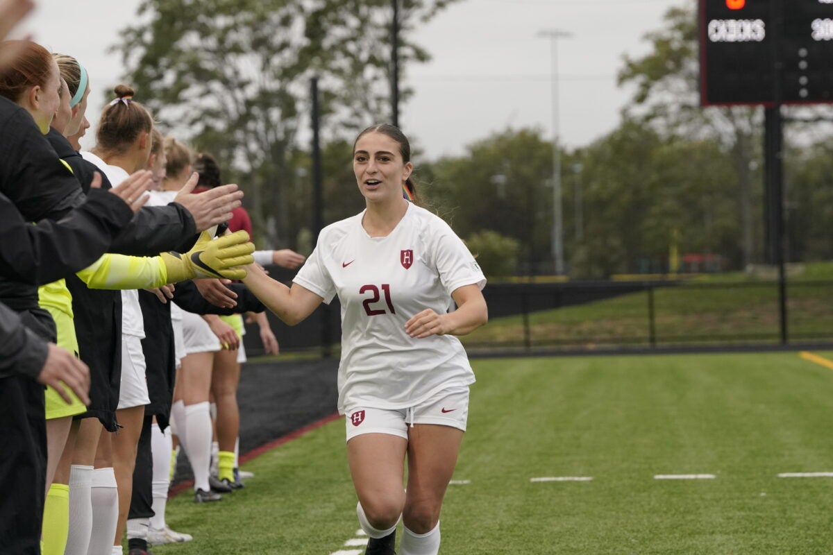 Female Harvard soccer player runs towards teammates to give a high five