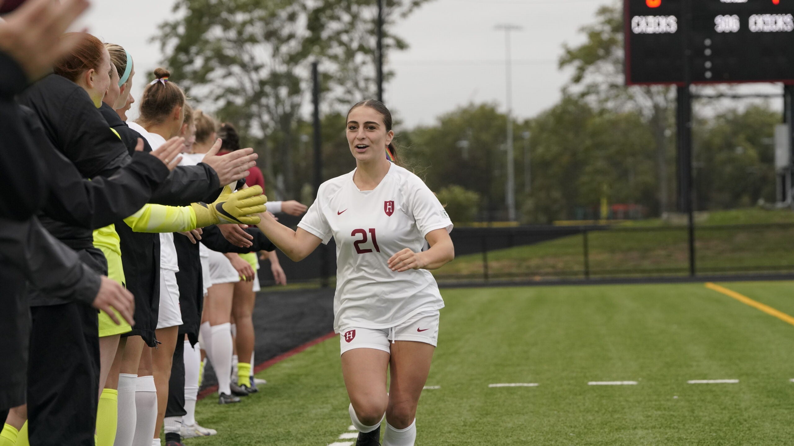 Female Harvard soccer player runs towards teammates to give a high five