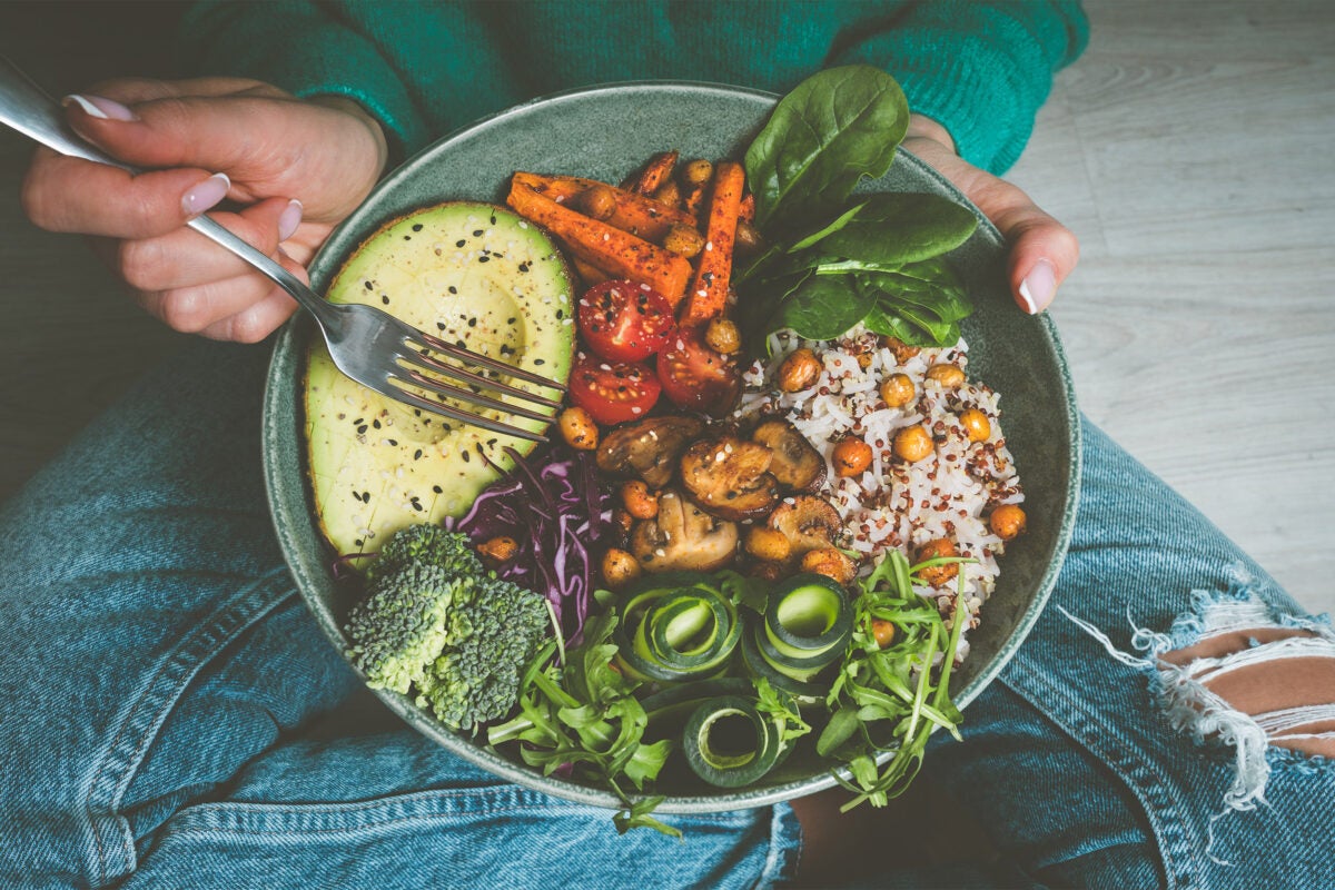 Woman eating bowl of food featuring healthy fats and carbs.