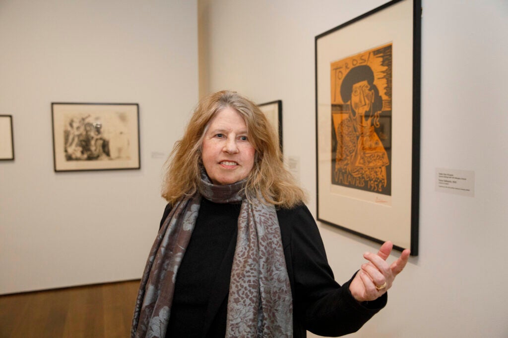 Suzanne Blier wearing a large scarf while pointing towards various Picasso artworks. 