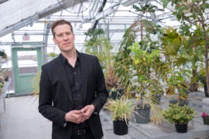 A man stands in a greenhouse with green plants behind him