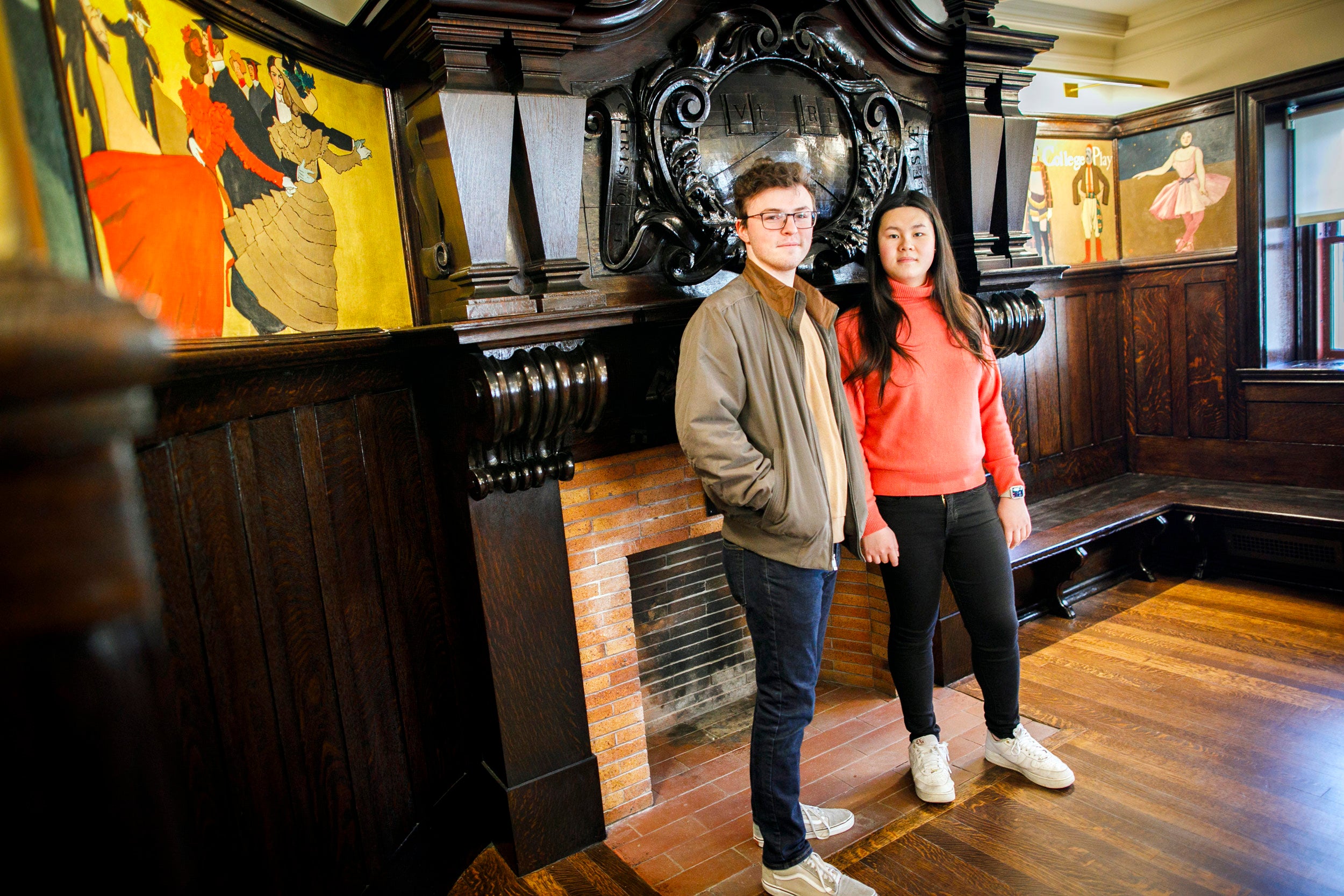Adams House’s House Committee Chairs (aka HoCos) Lily Liu and Tate Underwood share their favorite aspects of their student residence. Tate Underwood (left) and Lily Liu are pictured in the Coolidge Room by a fireplace decorated with a wooden carved veritas shield at Adams House.