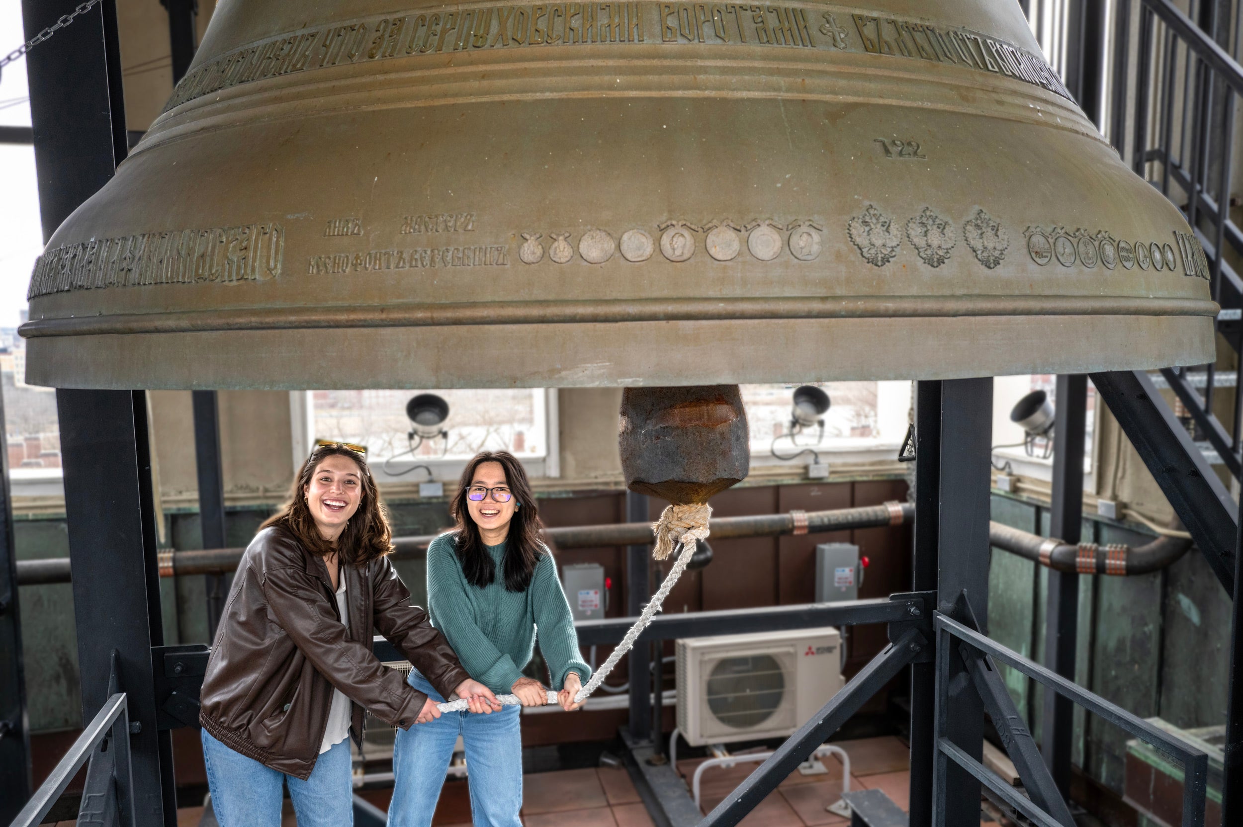 Sofia Giannuzzi (left) and Linh Vu ring a large bell in the Lowell House bell to