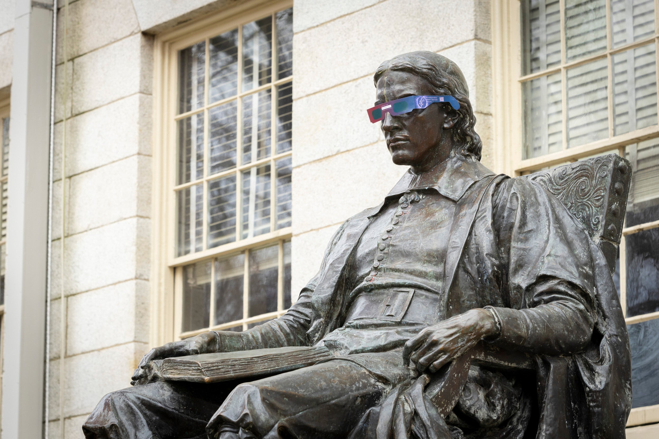 John Harvard statue wearing eclipse glasses.