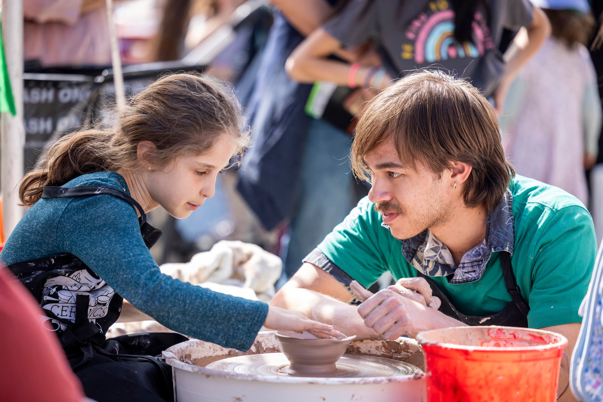 James Glaser ’25 helps a girl work on the pottery wheel on Science Center Plaza.