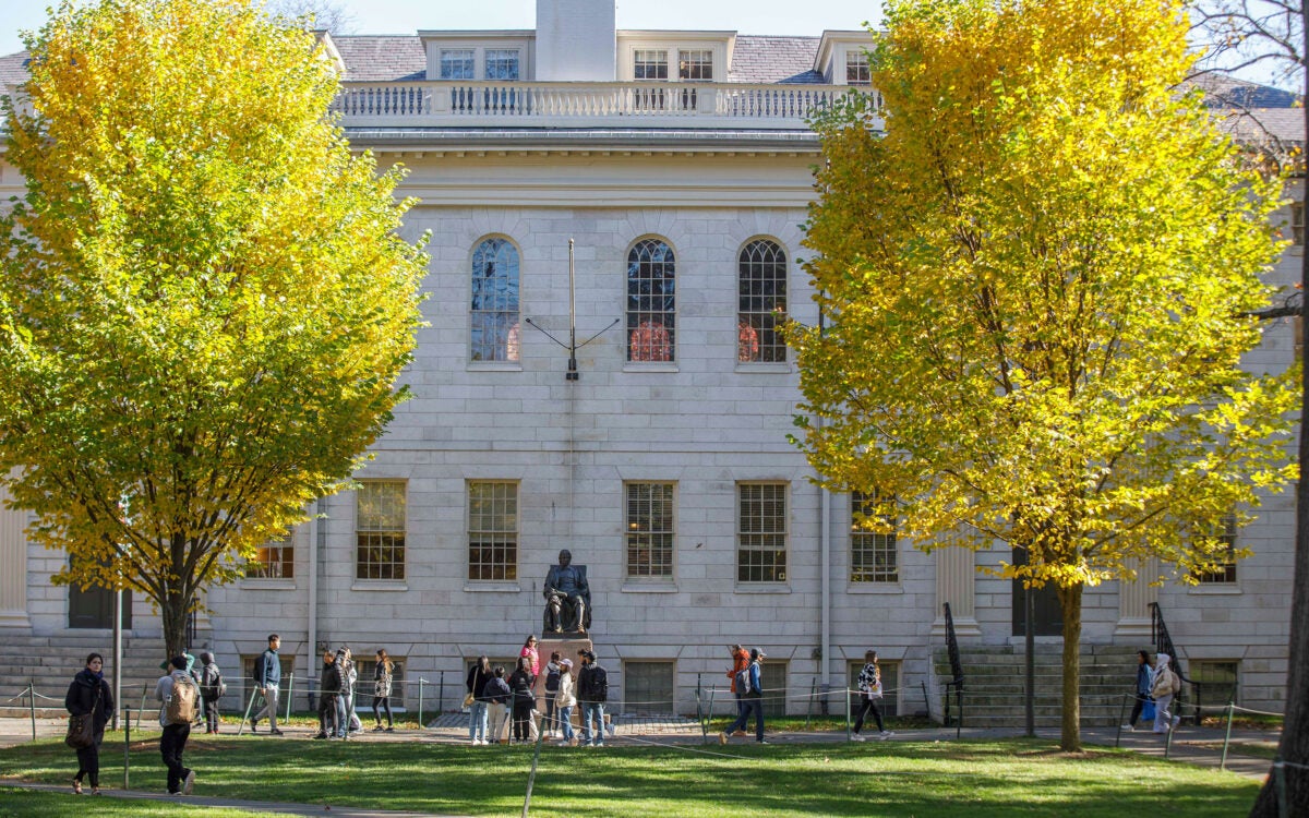 The John Harvard Statue and University Hall is flanked by Fall foliage during Autumn.