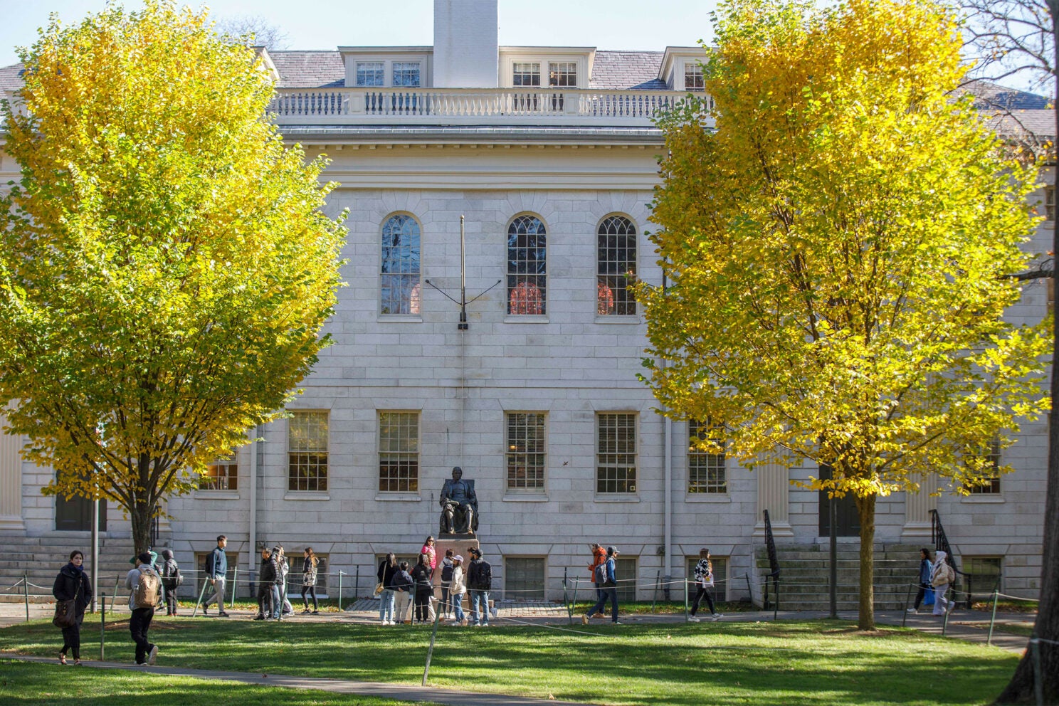 The John Harvard Statue and University Hall is flanked by Fall foliage during Autumn.
