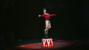 Performer Izzy Patrowicz wearing costume including top hat stands on a barrel at the circus.
