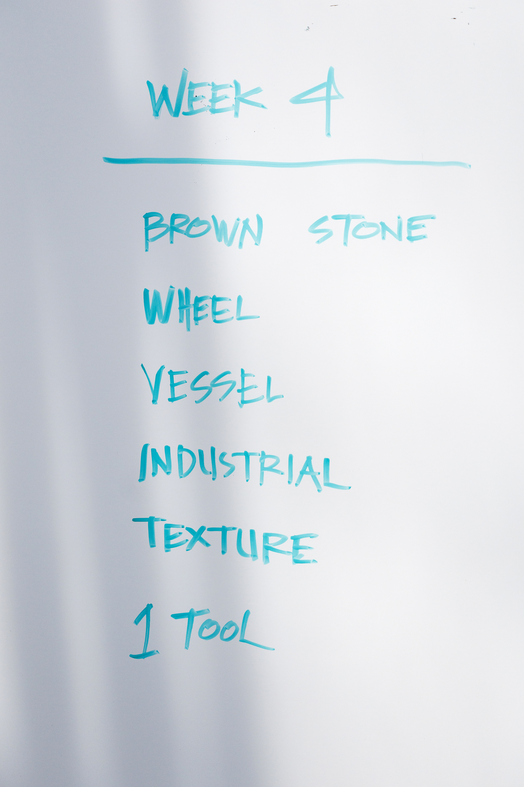 The Randomizer Week 4 directives - brown stone, wheel, vessel, industrial, texture, one tool - are outlined on a whiteboard.