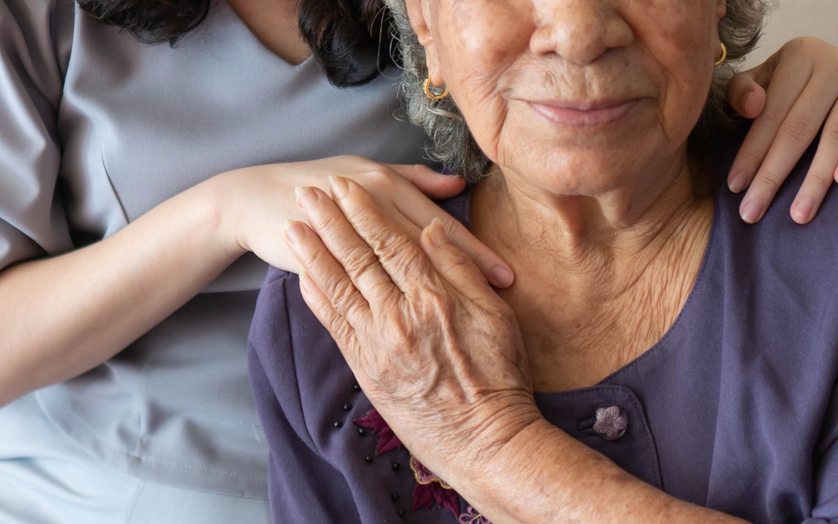 Woman putting her hands on an elderly woman's shoulder in sign of support.