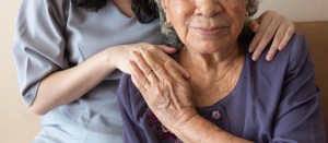 Woman putting her hands on an elderly woman's shoulder in sign of support.