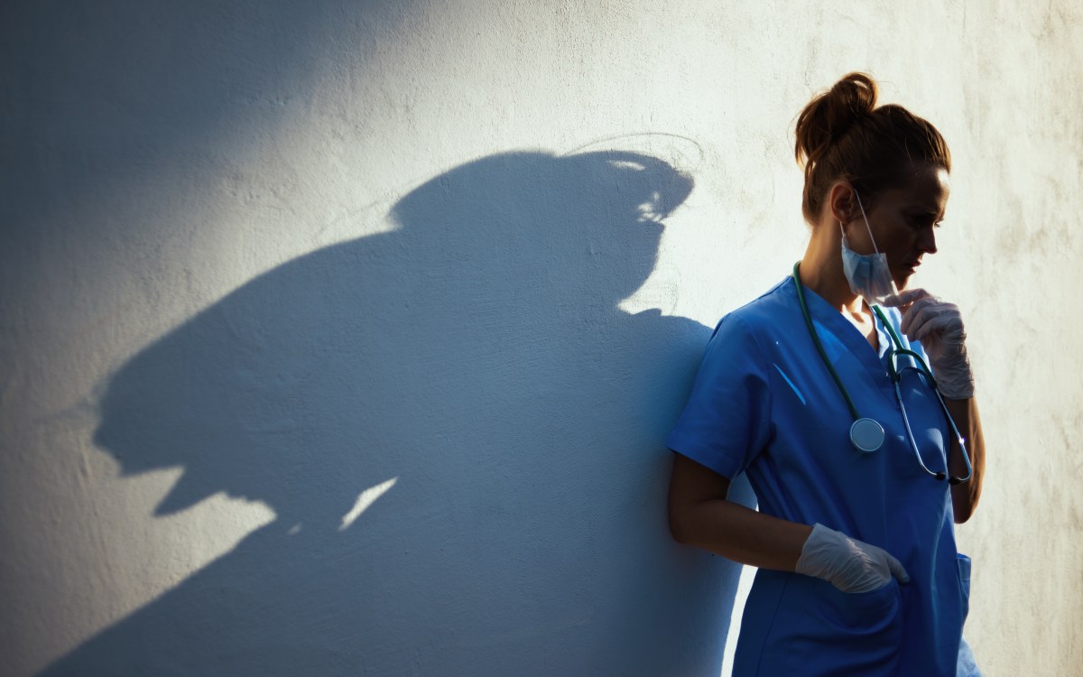 woman doctor standing in the shadows with her head tilted down.