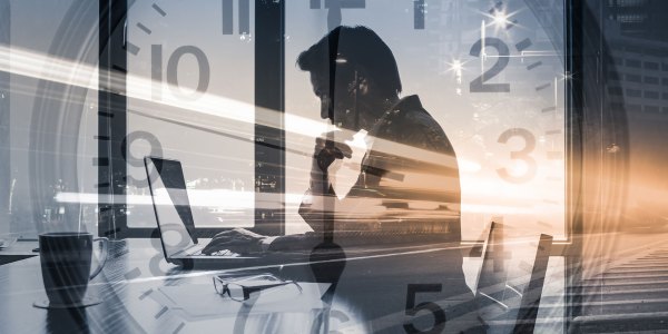Businessman sitting at desk and working with clock in background