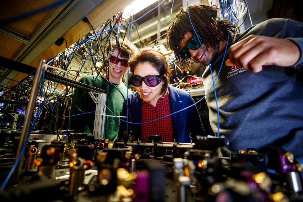 Quantum researchers Kang-Kuen Ni, Gabriel E. Patenotte, and Samuel Gebretsadkan peer at lenses and lasers in the lab.