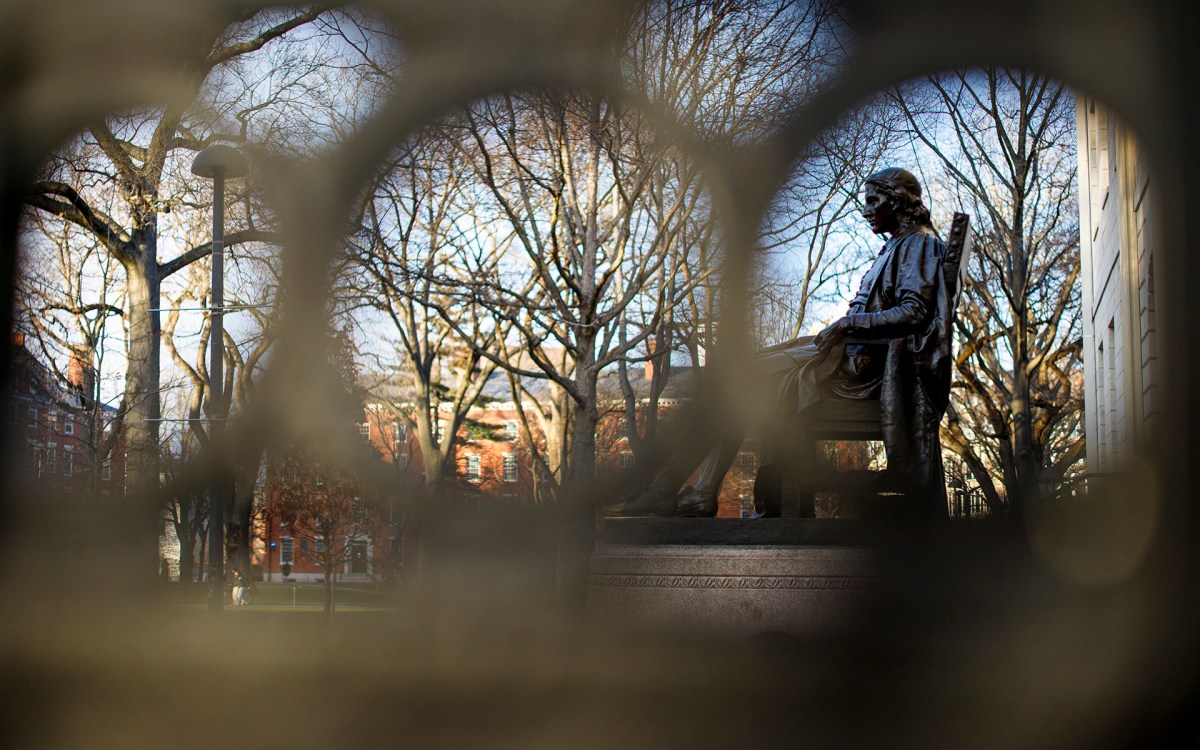 John Harvard statue as seen through the wrought iron rails of University Hall on Harvard's campus.