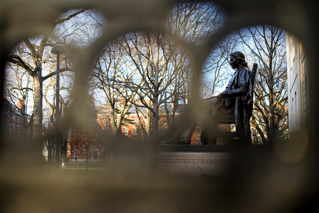 John Harvard statue as seen through the wrought iron rails of University Hall on Harvard's campus.