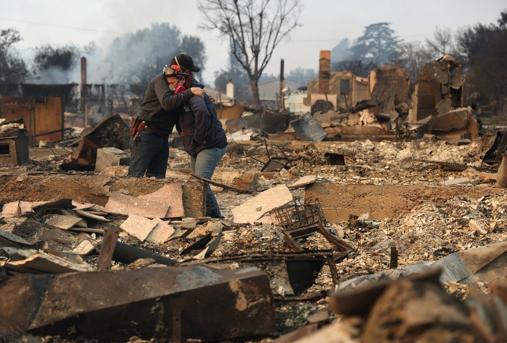 People embrace at the site of a family home destroyed by LA widlfire.