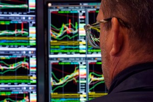 New York Stock Exchange tradre in front of computer screens showing economic graphs.