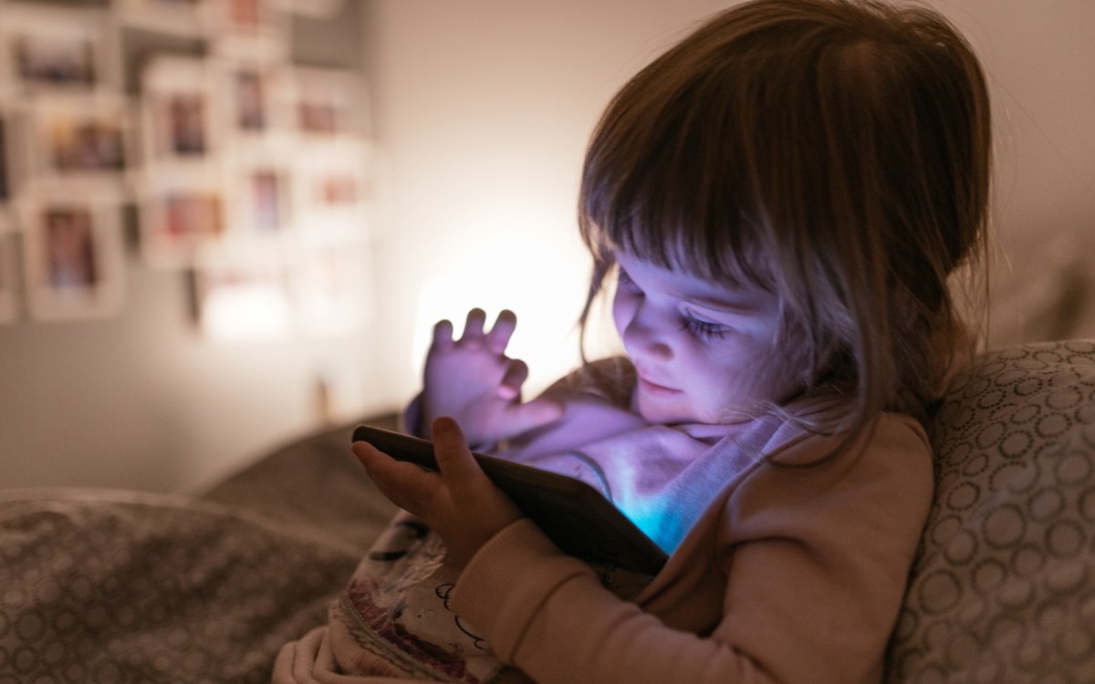 A child sits up in bed and plays on a cell phone.