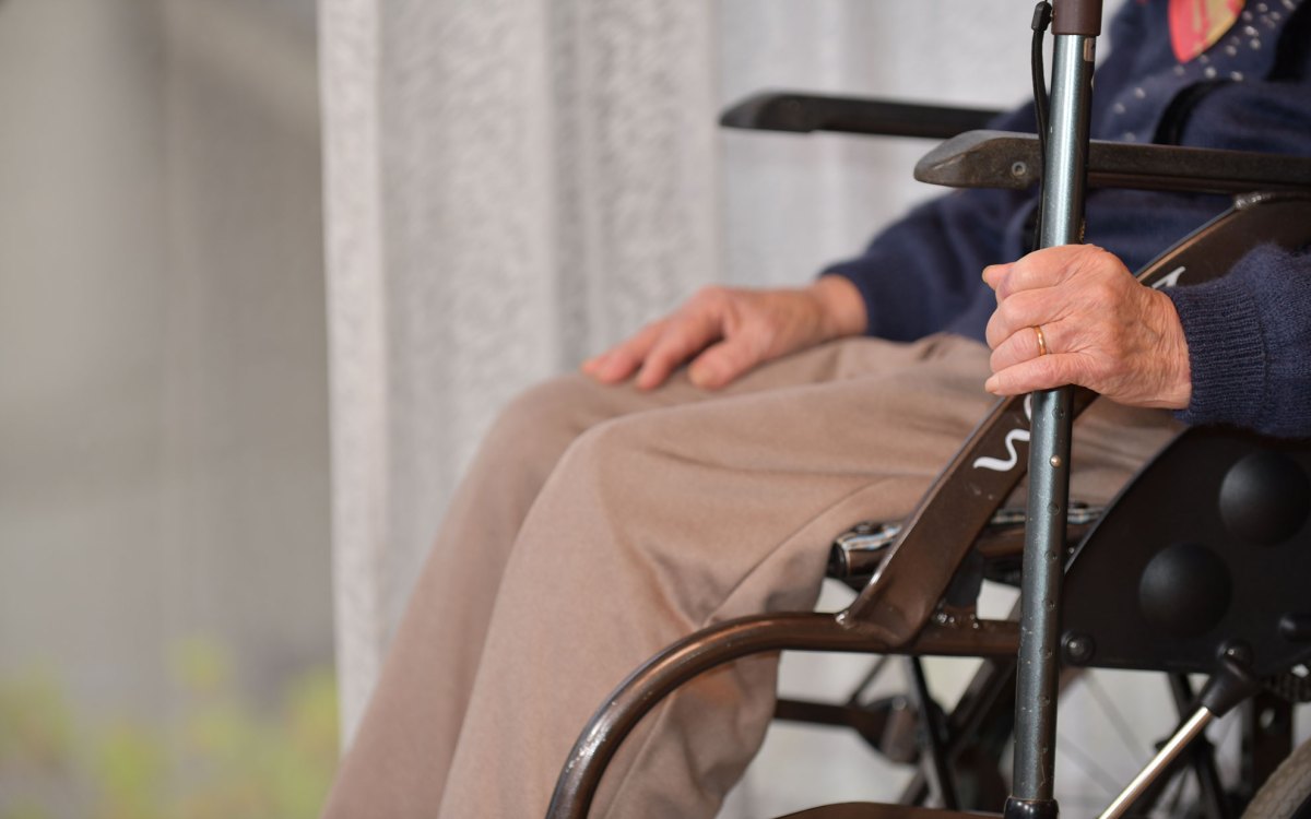 A senior woman sitting in a wheelchair with a cane.