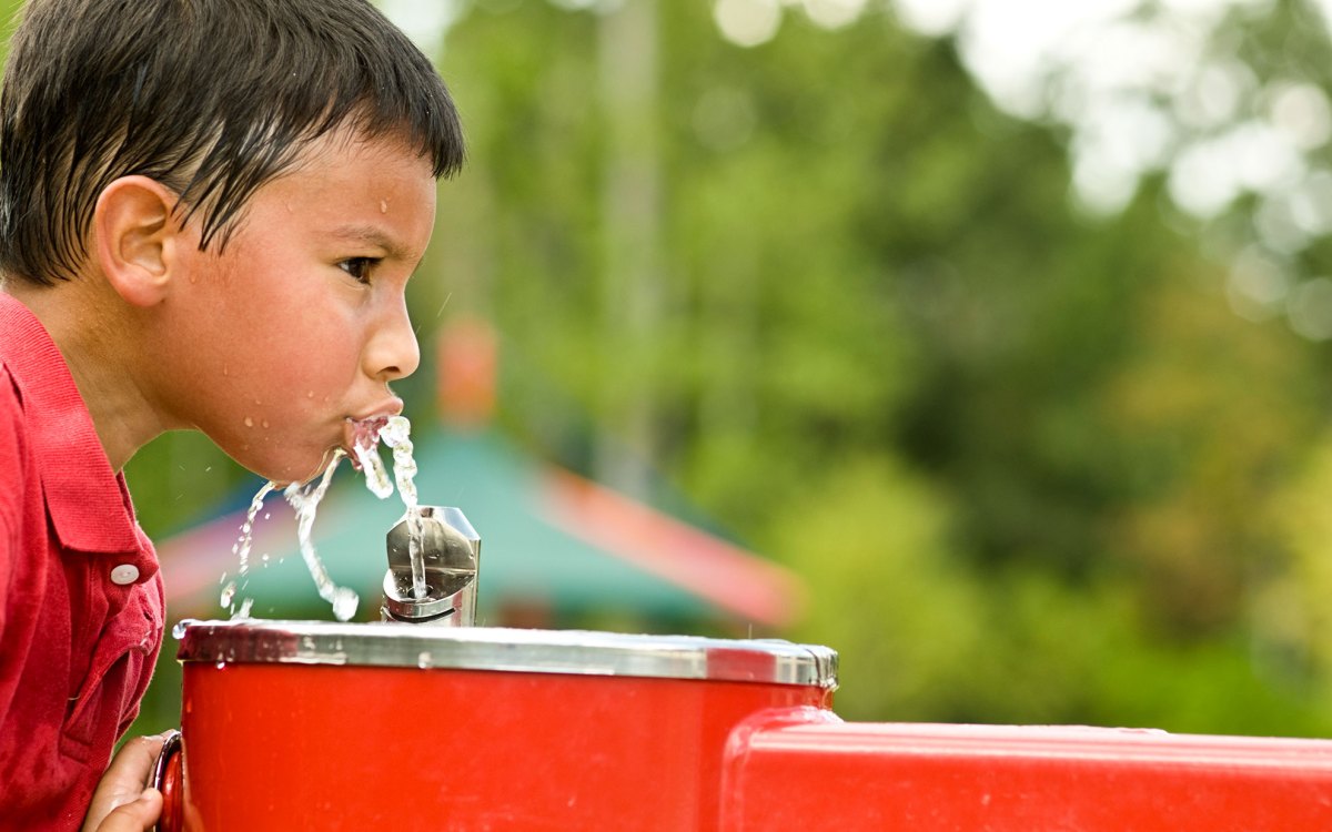Little boy getting heat relief from water fountain.