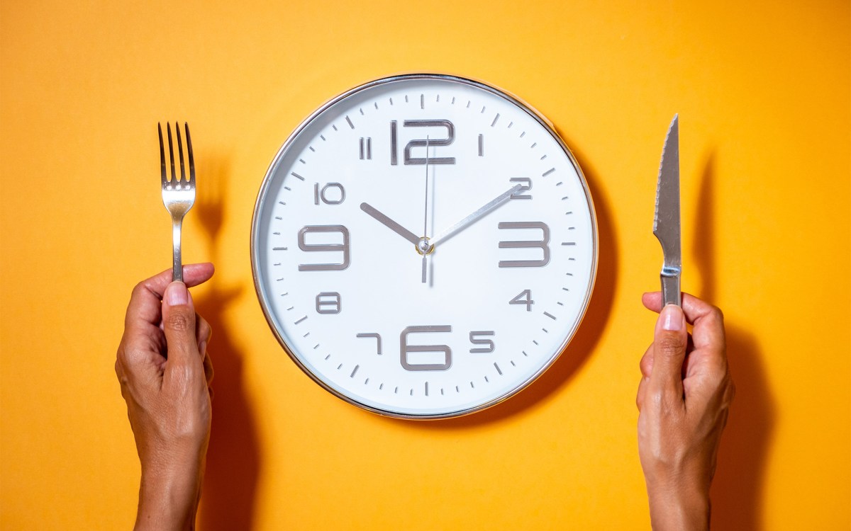 A clock as if it were a plate of food next to a hands holding fork and knife.