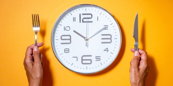 A clock as if it were a plate of food next to a hands holding fork and knife.