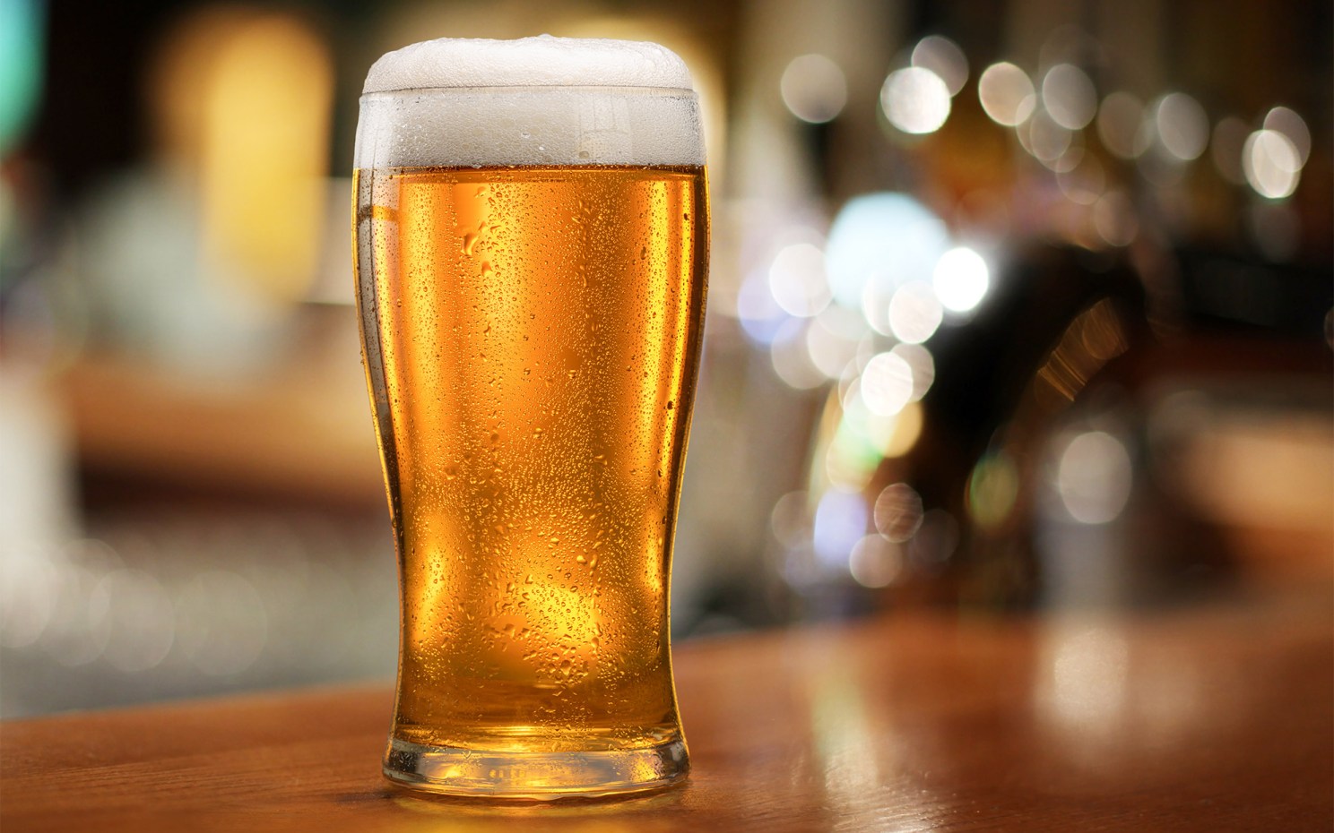 Glass of chilled beer on wooden bar table.