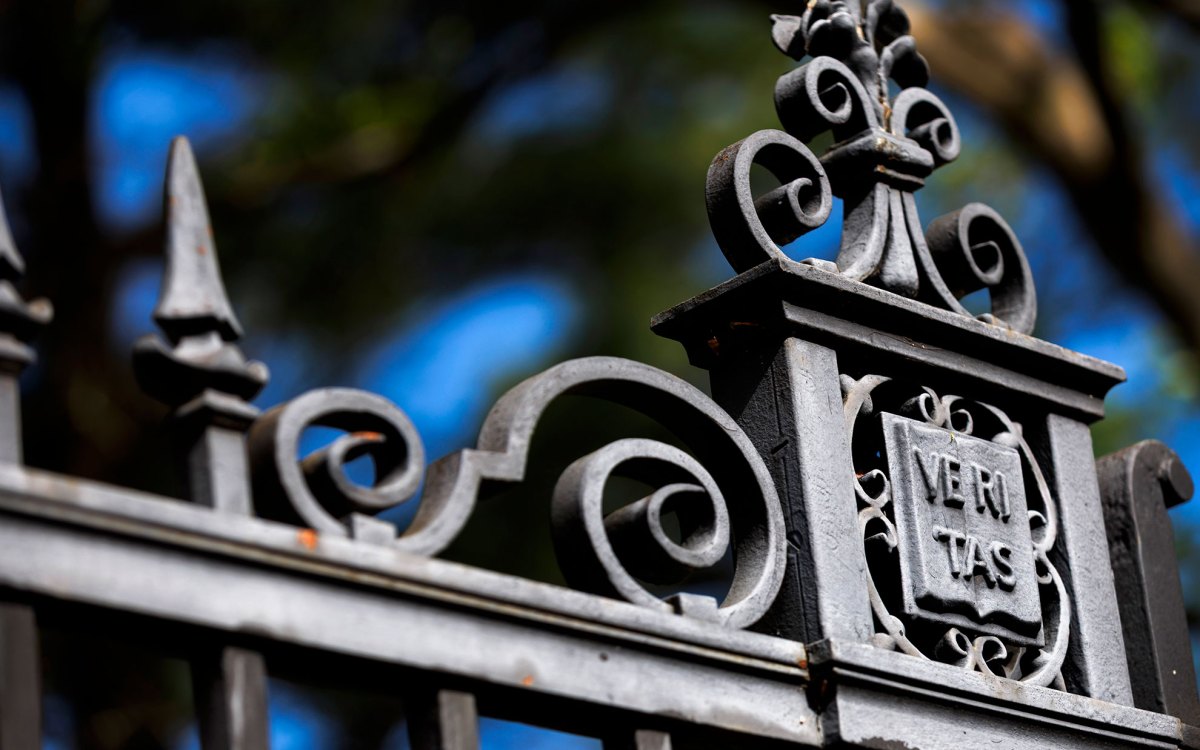 An ornate gate features a veritas shield alongside Harvard Yard.