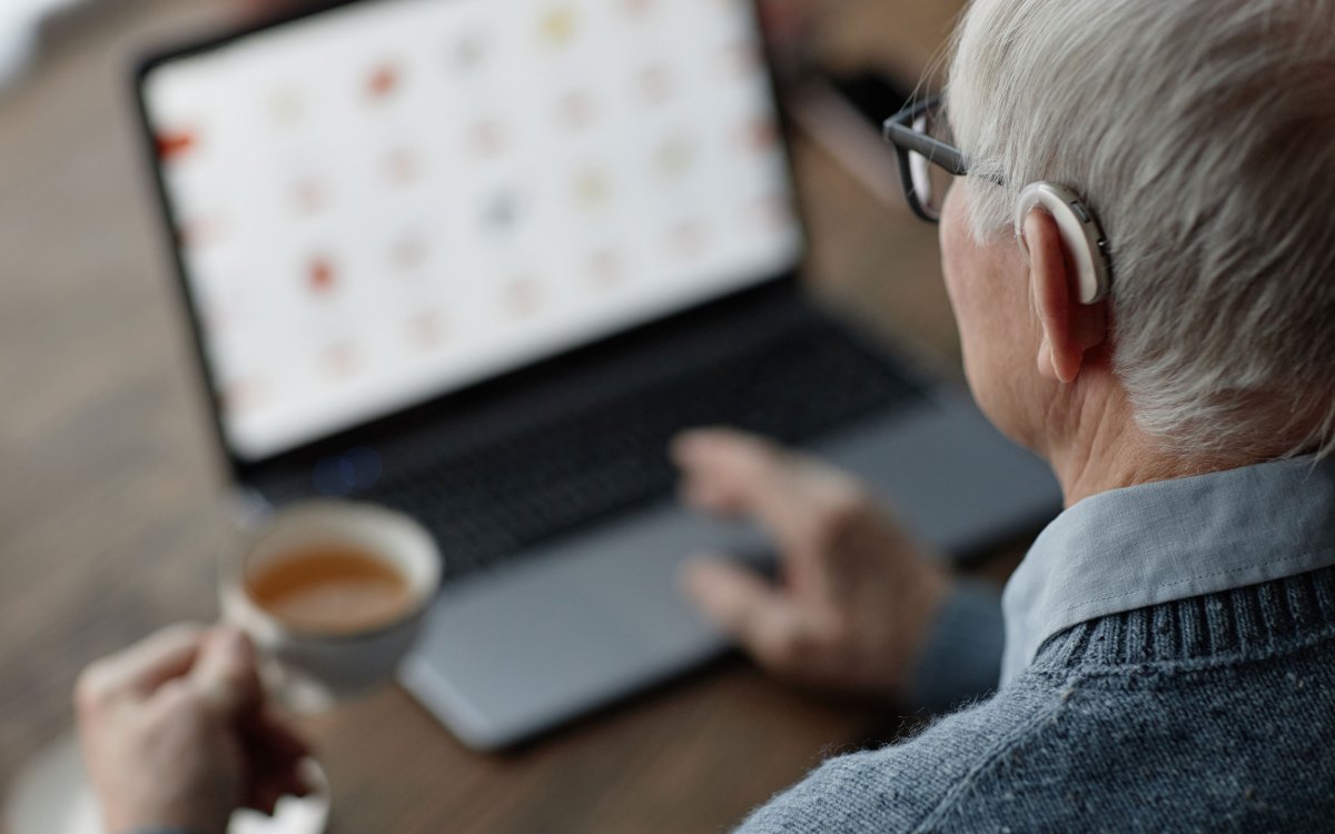Over shoulder shot of older man wearing hearing aid while working on laptop.